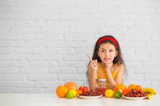 Thoughtful girl with colorful fresh fruits pointing upward