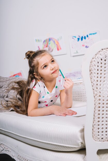 Thoughtful girl with pencil and blank paper on sofa