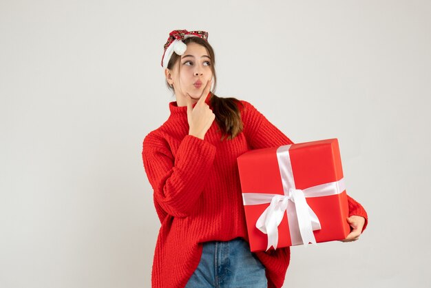 thoughtful girl with santa hat holding her gift standing on white