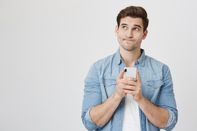 Thoughtful guy looking up, holding mobile phone