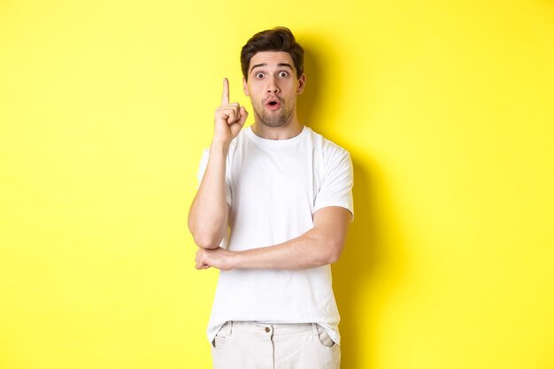 Вдумчивый парень предлагает решение, поднимает палец в знак эврики и выглядит взволнованным, у него есть идея, стоя на желтом фоне.