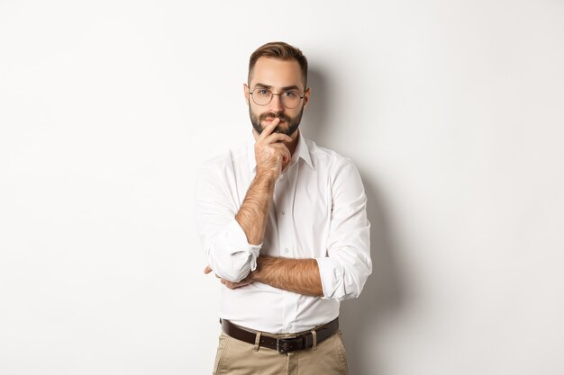 Thoughtful handsome businessman looking at camera, making choice or thinking, standing in glasses