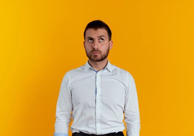 Thoughtful handsome man looks up isolated on orange wall