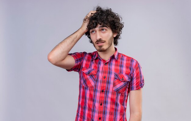 A thoughtful handsome man with curly hair in checked shirt holding hand on head 