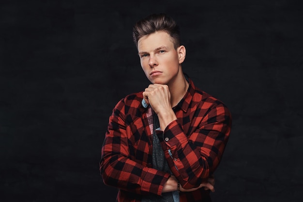 Thoughtful handsome young guy in a fleece shirt, posing with hand on chin at a studio. Isolated on a dark background.