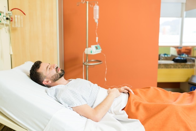 Задумчивый больной пациент с кислородом лежит на больничной койке во время лечения