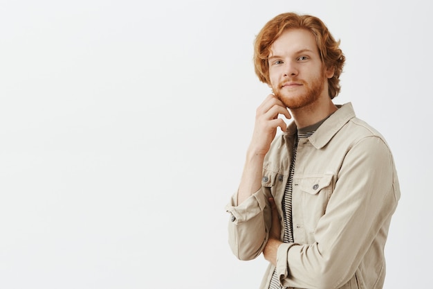 Free photo thoughtful and intrigued bearded redhead guy posing against the white wall