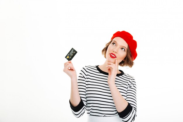 Thoughtful lady holding credit card and looking up