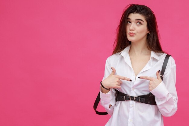 Thoughtful lady pointing her fingers to each others and standing on pink background