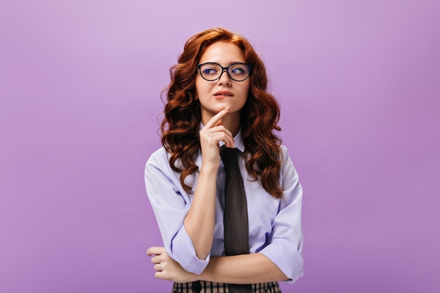 Thoughtful lady in shirt and eyeglasses poses on purple wall