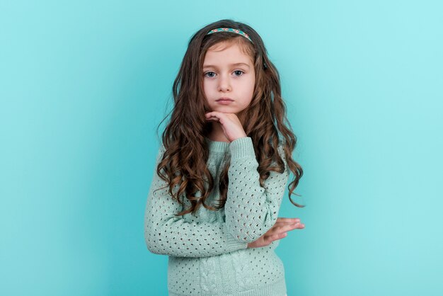 Thoughtful little girl standing on blue background 