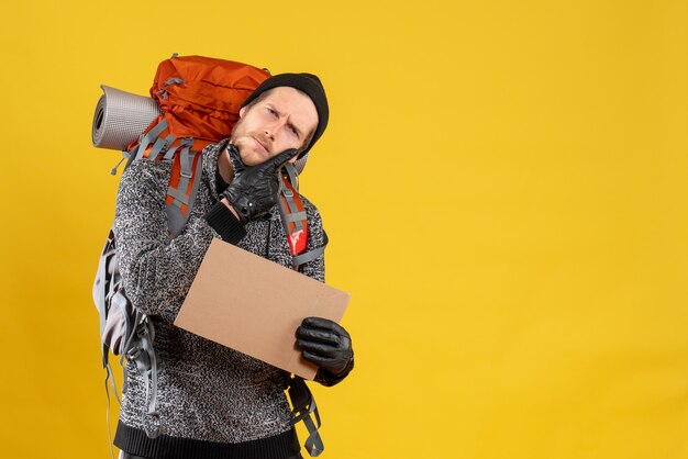 thoughtful male hitchhiker with leather gloves and backpack holding blank cardboard