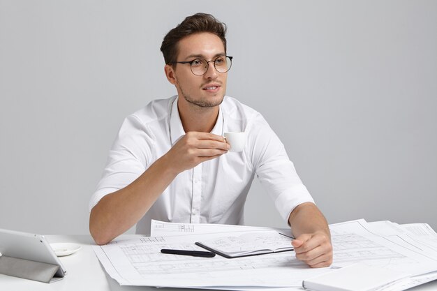 Thoughtful male manager keep cup of coffee, looks pensively into distance, plans his future actions, thinks how to draw template on webpage, has great ideas in mind. Designing and construction concept