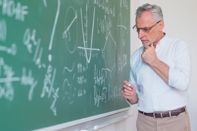 Thoughtful male teacher standing at blackboard and keeping chalk