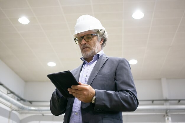 Free photo thoughtful man in protective helmet holding tablet and looking at screen