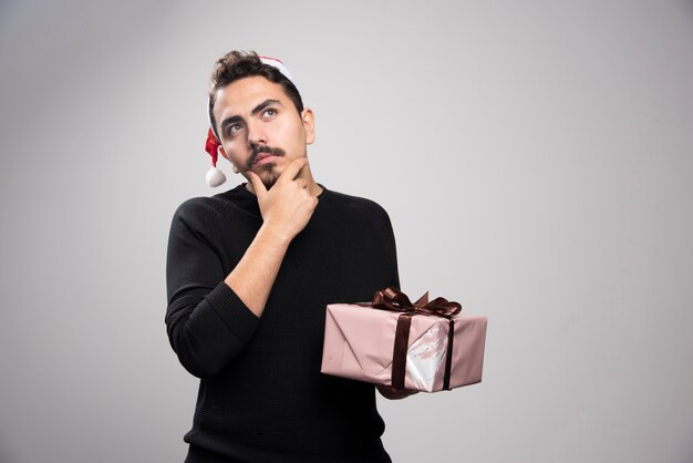 A thoughtful man in a Santa's hat holding a New Year's gift .