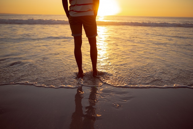 Вдумчивый человек, стоящий с руками в кармане на пляже