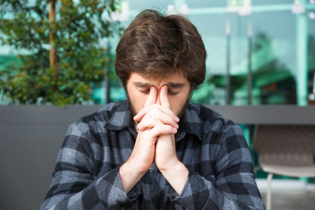 Thoughtful man touching nose bridge and thinking in street cafe