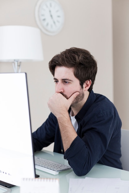 Бесплатное фото Задумчивый человек, используя компьютер в офисе