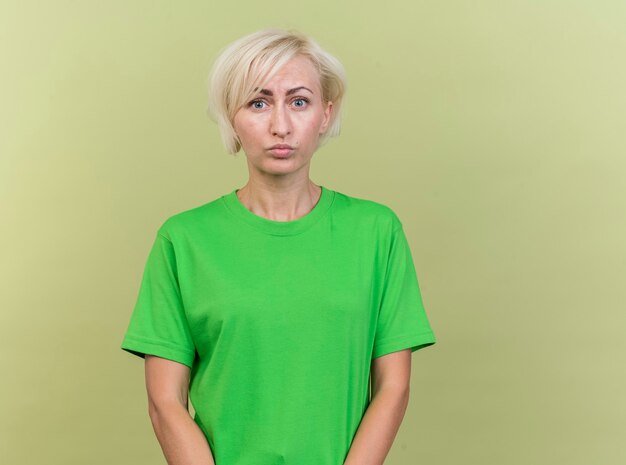 Free photo thoughtful middle-aged blonde slavic woman looking at camera isolated on olive green background with copy space