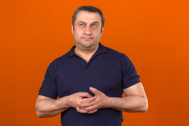 Thoughtful middle aged man wearing polo shirt looking up and thinking over isolated orange wall