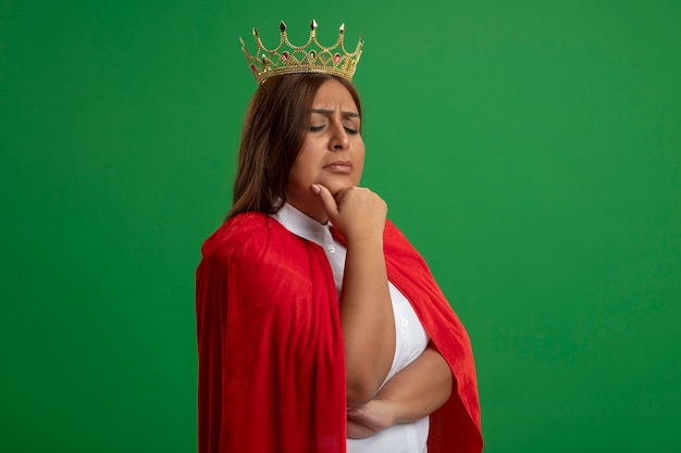 thoughtful middle-aged superhero female looking down wearing crown grabbed chin isolated on green