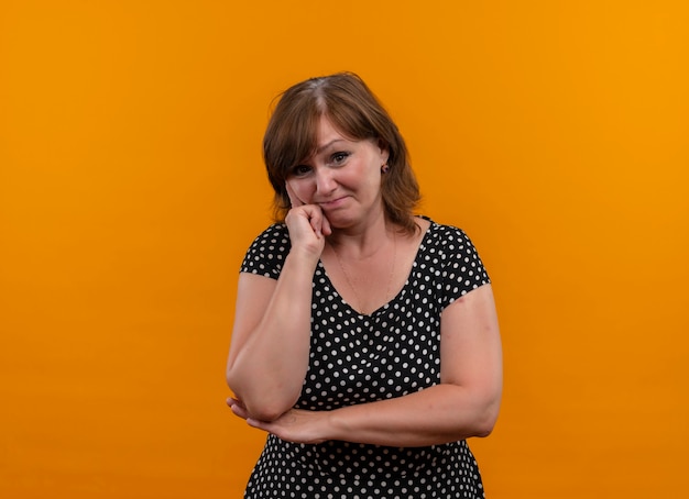 Thoughtful middle-aged woman putting finger on cheek on isolated orange wall with copy space