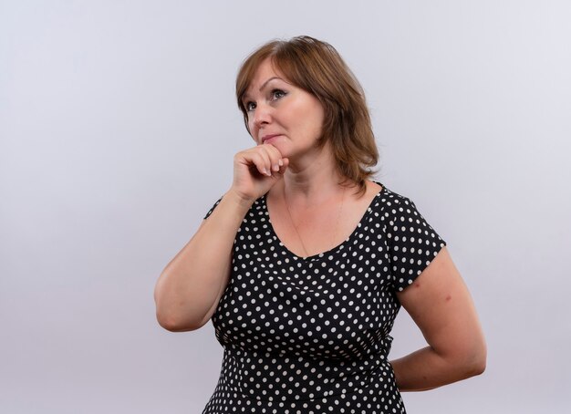 Thoughtful middle-aged woman putting hand on chin on isolated white wall