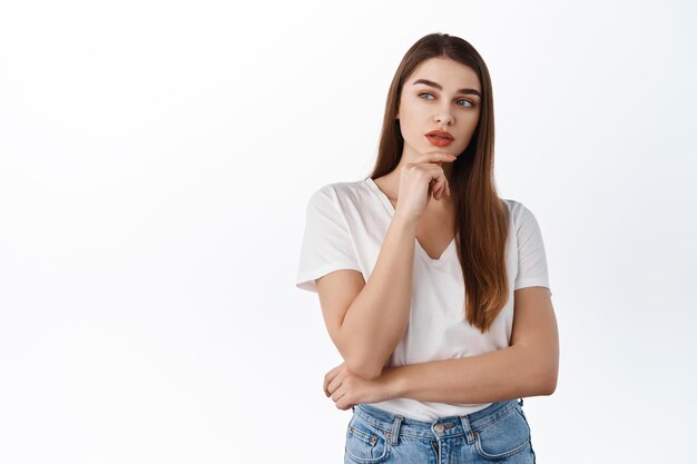 Thoughtful modern girl making choice, look pensive aside at copyspace, deciding, thinking about something, standing over white background