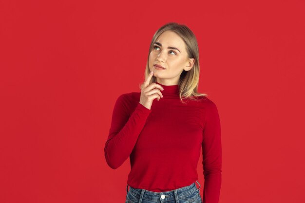 Thoughtful. Monochrome portrait of young caucasian blonde woman isolated on red wall. Beautiful female model in shirt. Human emotions, facial expression, sales, ad concept. Youth culture.