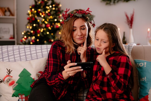 thoughtful mother and daughter looking at phone sitting on couch and enjoying christmas time at home