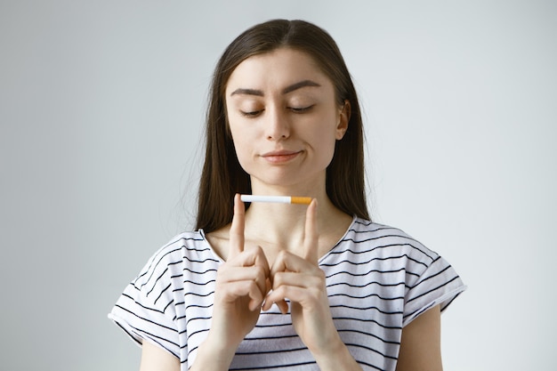 Free photo thoughtful pensive young european woman facing hard choices, holding cigarette between two index fingers