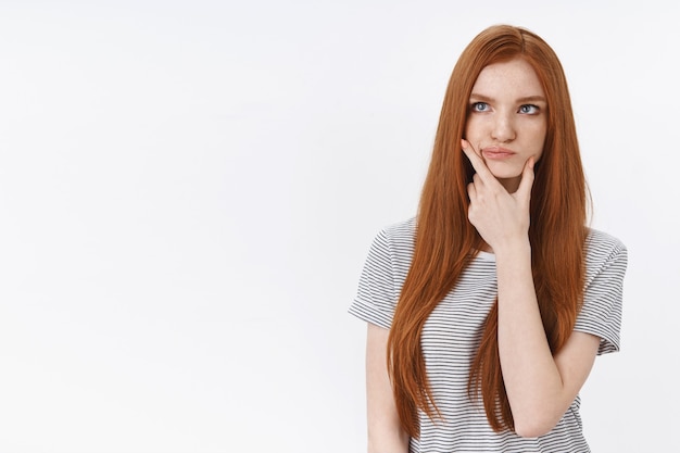 Thoughtful perplexed pondering young redhead blue-eyed woman smirking touching jawline thinking look upper left corner hesitant have doubts, standing white wall unsure
