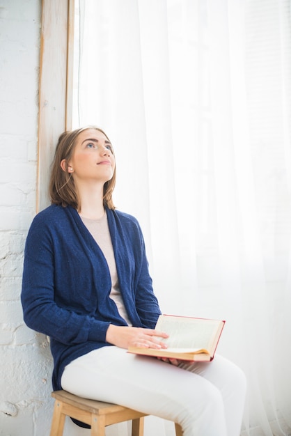 Thoughtful pretty woman at home holding book