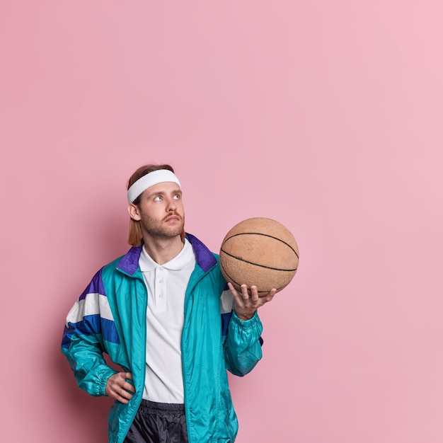 Thoughtful professional basketball player in activewear holds ball concentrated above going to play favorite game.