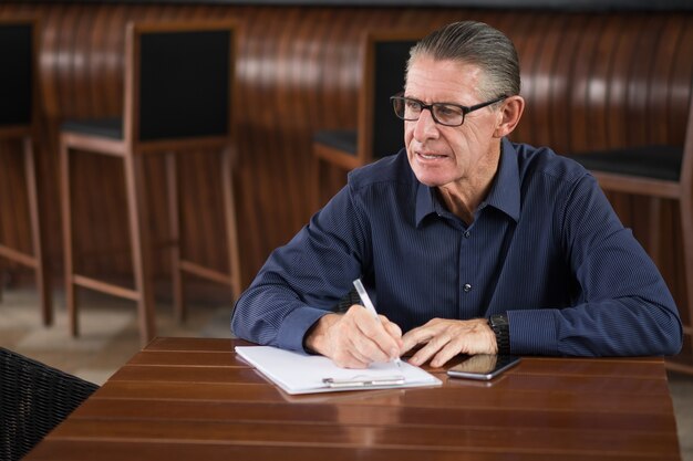 Thoughtful Senior Man Writing Notes in Restaurant