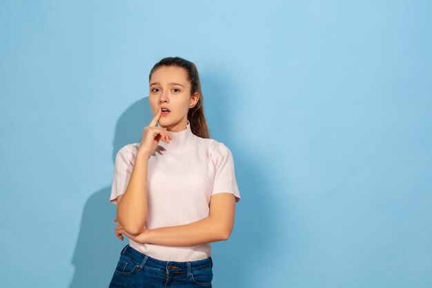Thoughtful, serious. Caucasian teen girl's portrait on blue background. Beautiful model in casual wear. Concept of human emotions, facial expression, sales, ad. Copyspace. Looks cute, astonished.