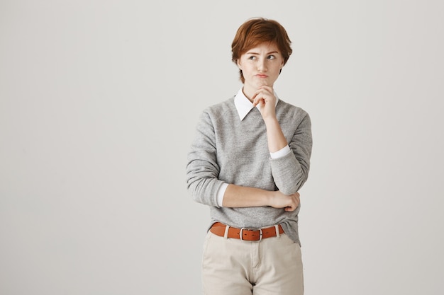 Thoughtful serious redhead girl with short haircut posing against the white wall