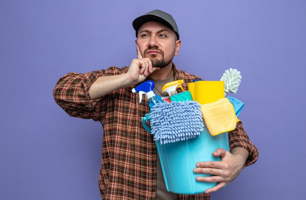 Thoughtful slavic cleaner man holding cleaning equipment and looking at side