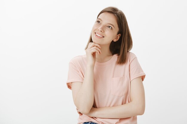 Thoughtful smiling woman looking upper left corner dreamy, tempted to try something