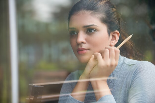 Thoughtful student holding pencil behind glass