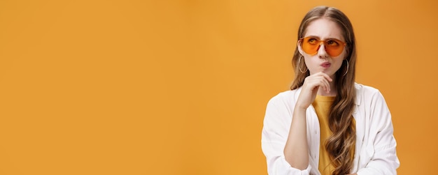 Thoughtful stylish party girl with long wavy natural hairstyle in trendy sunglasses and blouse smirk