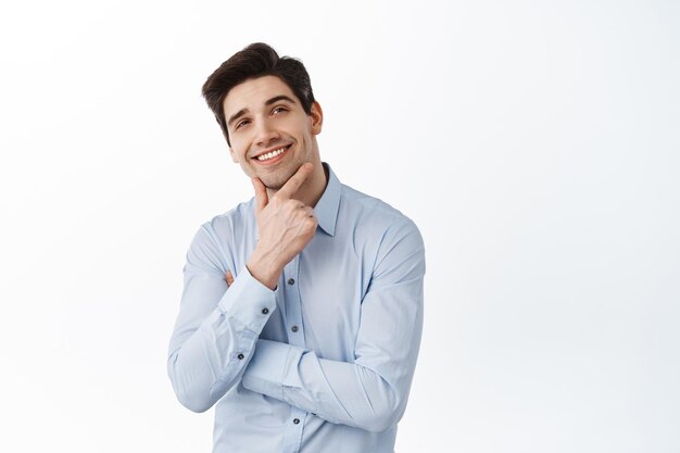 Thoughtful successful businessman, ceo manager look aside and thinking, imaging something with pleased face, smiling, standing over white background