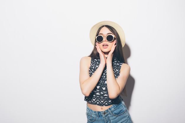Задумчивая летняя женщина в шляпе и солнцезащитных очках, изолированные на белой стене