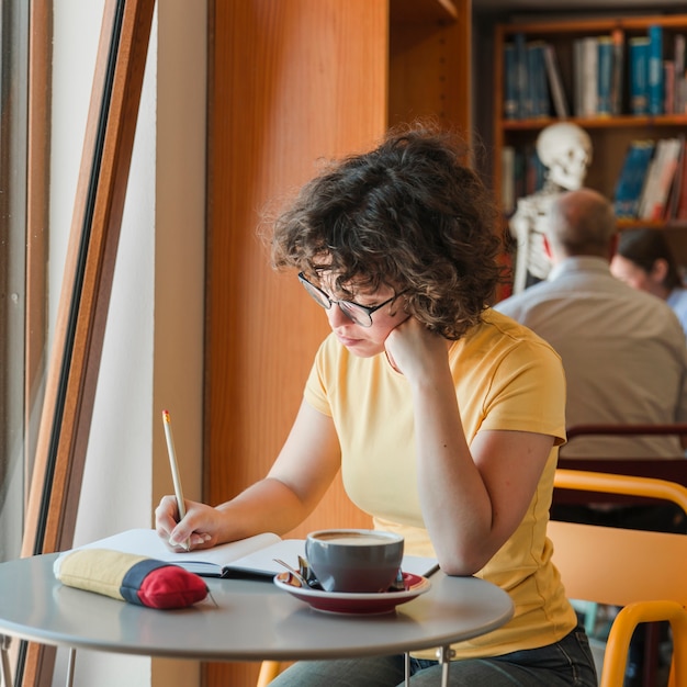 思いやりのある十代の少女は、ウィンドウの近くのメモ帳で書く