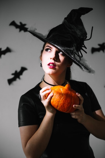 Free photo thoughtful witch with pumpkin looking up