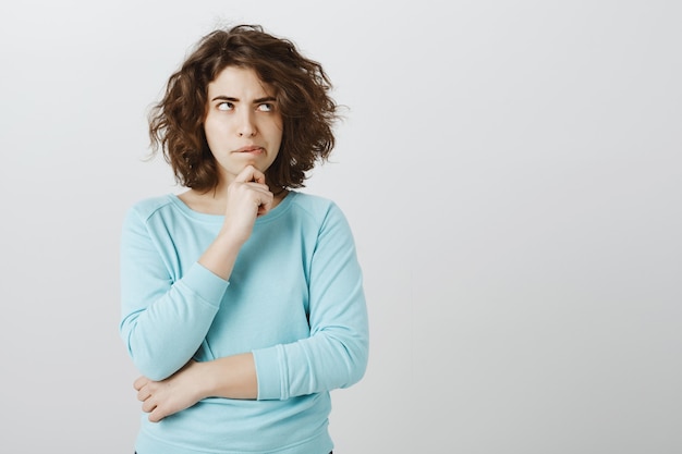 Thoughtful woman biting lip and looking up while making idea, have important decision