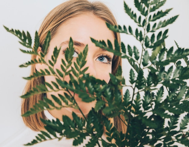 Thoughtful woman covering face with fern leaves 