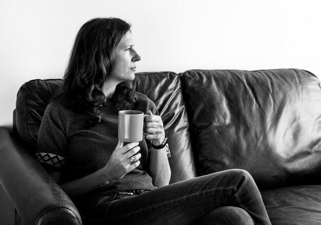 Задумчивая женщина, пить чай или кофе, сидя на уютном диване