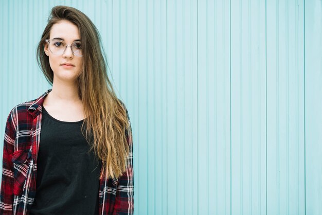 Thoughtful woman in glasses standing at blue wall